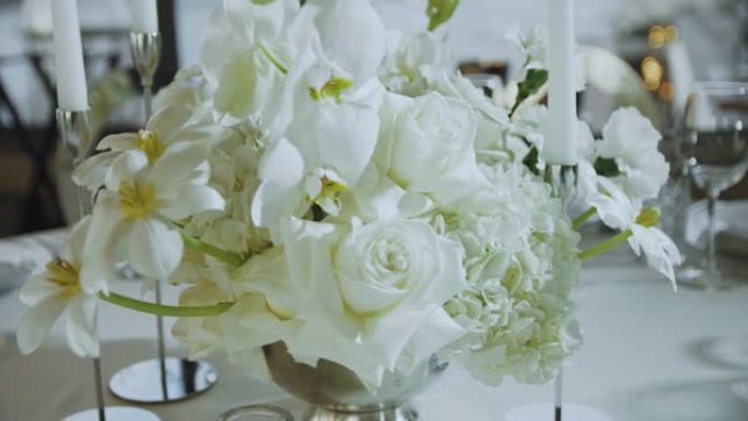 婚礼上的花卉装饰。餐厅的桌子上摆着白色的鲜花。玫瑰和蜡烛的花的美丽排列。慢动作。
