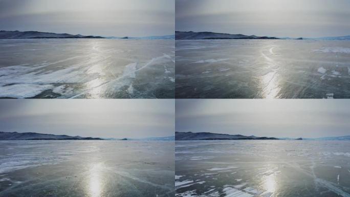 在贝加尔湖裸露的冰面上剧烈飞行，太阳在表面反射，山脉在背景中。俄罗斯西伯利亚贝加尔湖。无人机航拍4k