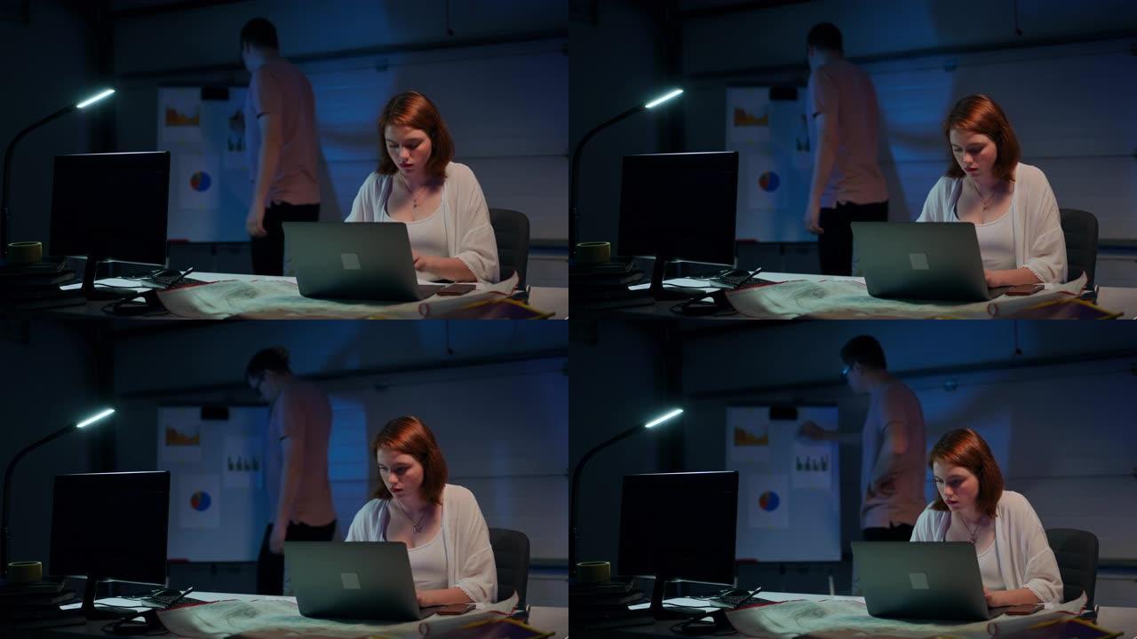自信的专注女性在笔记本电脑上在线传递信息的肖像，模糊的男人正在分析背景白板上的文书工作。美丽的启动与