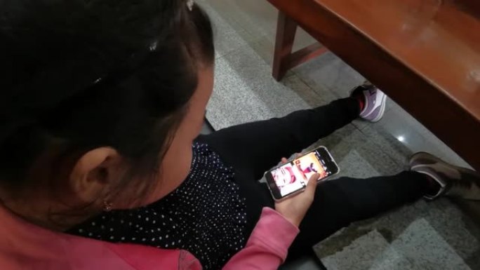 胖乎乎的小女孩拿着移动智能手机，着迷于查看教堂内的社交媒体应用程序内容。