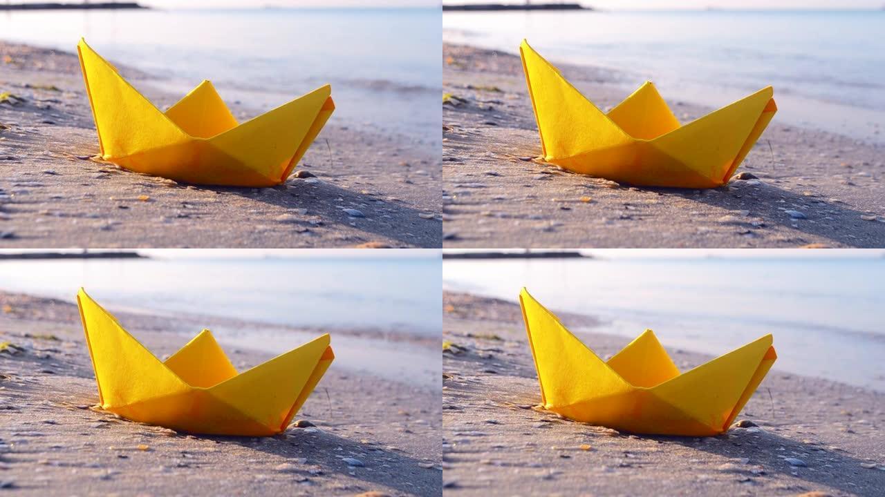 小纸黄船在海浪背景上靠近水面的沙子上特写。沙滩上的纸船夏天阳光明媚的日子。概念冒险旅行度假假期休息旅