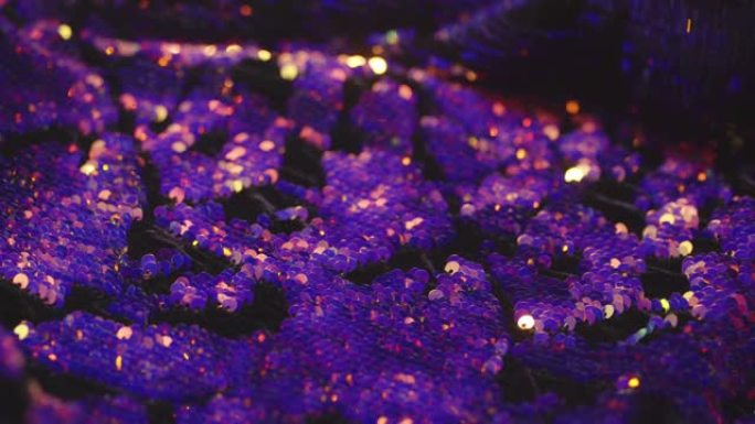 裁缝手中的服装面料上的紫色和金色亮片宏观，明亮地反射光线，变色4K