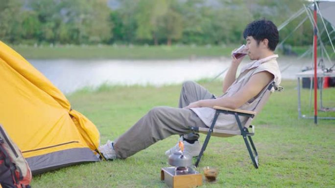 4K，亚洲年轻人在暑假旅行假期放松并享受在森林山露营的户外生活方式。有吸引力的男性喝咖啡，而喜欢在绿