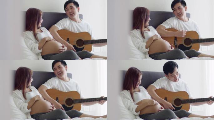 快乐的亚洲丈夫和怀孕的妻子在卧室里共度时光，丈夫弹吉他唱歌。