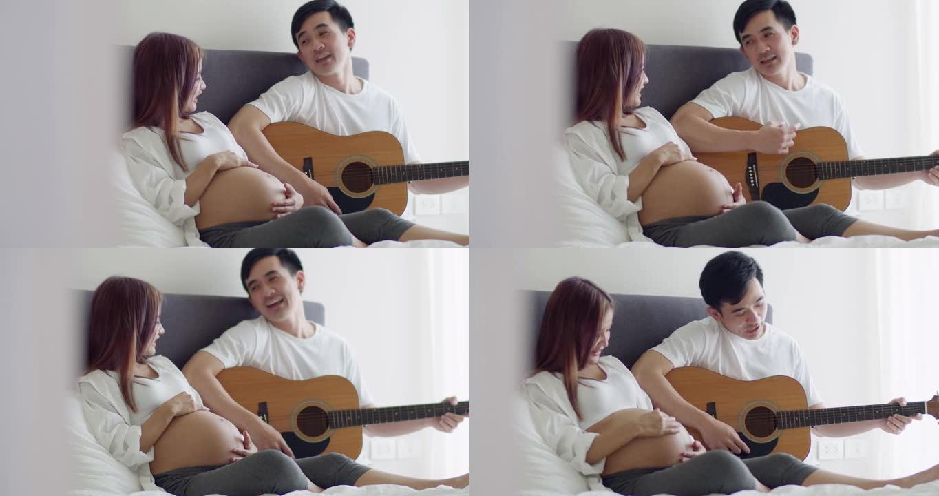 快乐的亚洲丈夫和怀孕的妻子在卧室里共度时光，丈夫弹吉他唱歌。