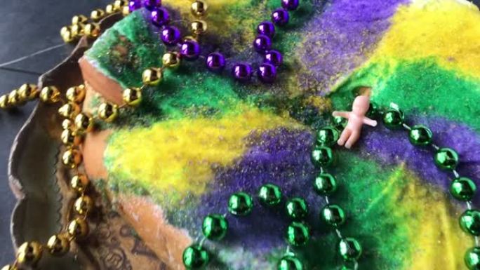 旋转放大在Mardi Gras国王蛋糕和小宝宝被彩色珠子包围在古董托盘上
