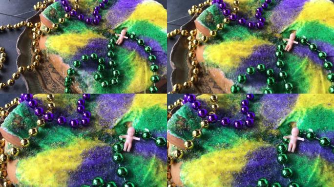 旋转放大在Mardi Gras国王蛋糕和小宝宝被彩色珠子包围在古董托盘上