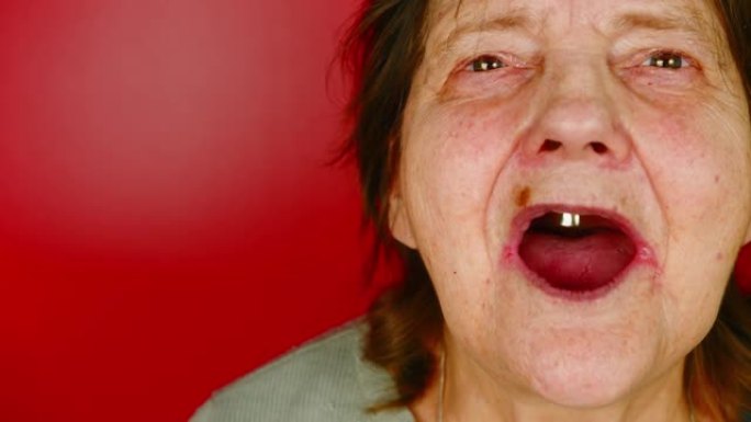 红色背景上的成熟女人。祖母嘴里含着一颗牙齿笑的肖像。年龄相关变化的概念