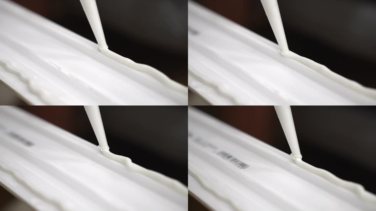 用工业管在白色踢脚线表面上应用之字形胶水的多利射击，用于建筑工地底座安装的白色密封胶，使用粘合材料进