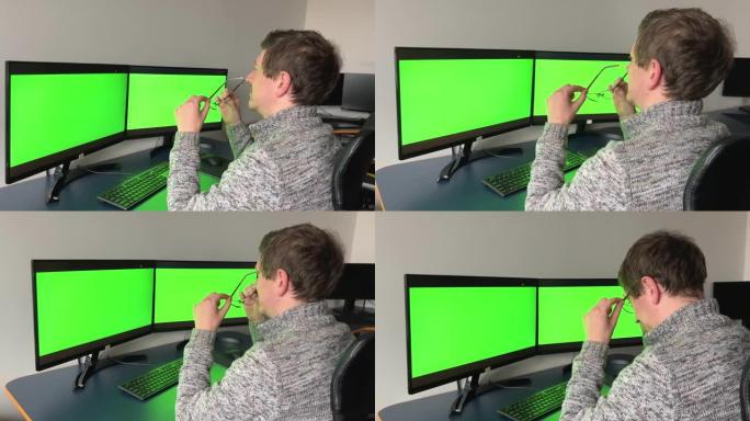 两个监视器的特写绿屏黑暗中的男人坐在后面的广告光学空间用于文本在线培训计算机程序疲劳休息时间即将旅行