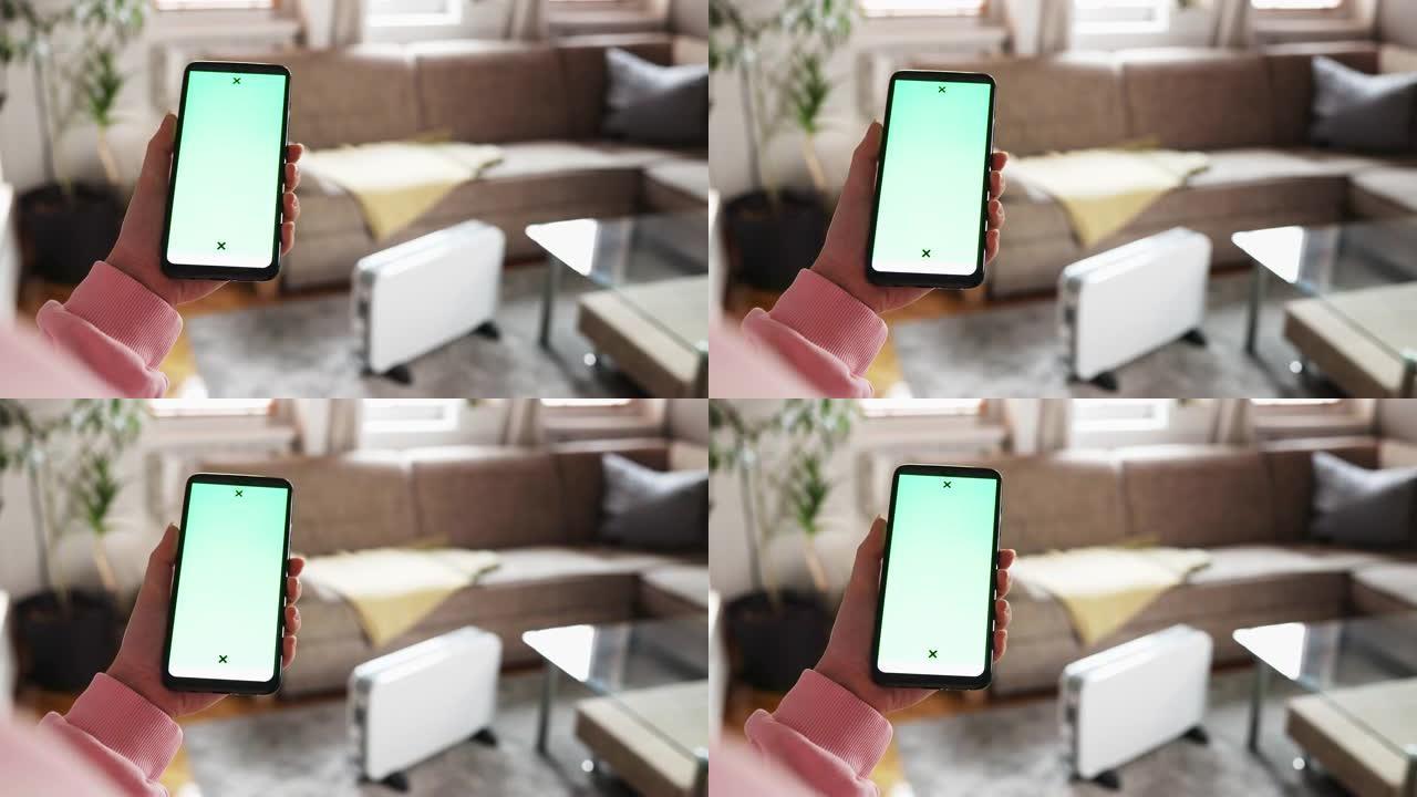 女性手的特写显示屏幕上带有模型的智能手机。客厅背景中的散焦电加热器。现代公用事业账单应用程序和供暖季