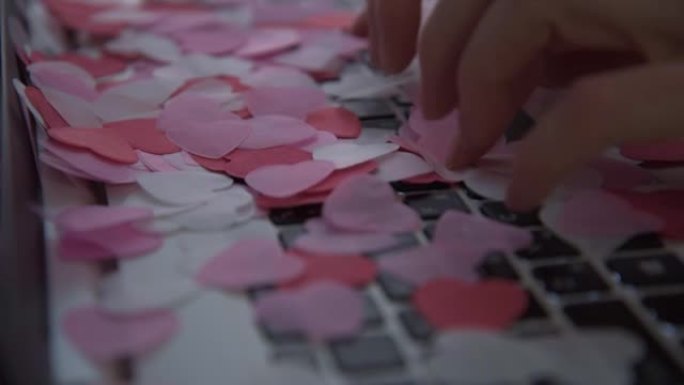 妇女的手在笔记本电脑键盘上打字。心形的五彩纸屑开始从上面倾泻。情人节祝贺的概念。情书的概念。电子形式