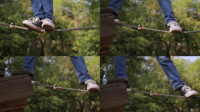 在冒险公园里，一个穿着运动鞋的男孩的特写镜头正在绳索路上攀爬。