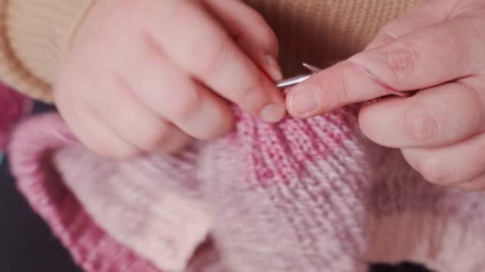 女性手中的织针特写，编织粉红色纱线织物