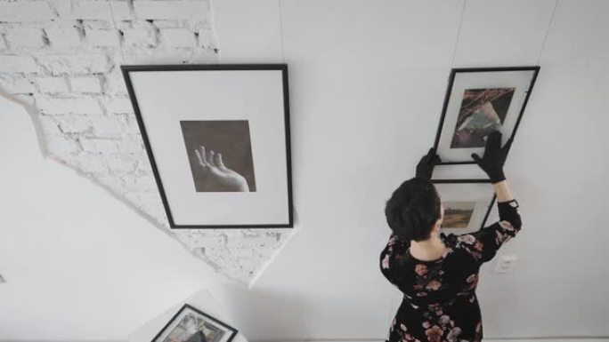 一位女画廊主在展厅的墙上悬挂着新的绘画和拼贴画。当代艺术专家在画廊工作，并准备新的展览和拍卖。