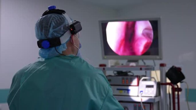 医生背对着镜头站着，看着屏幕。进行手术的外科医生看着显示内部器官的屏幕。特写。