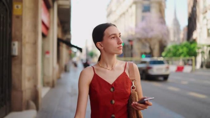 美丽的年轻女子走路，看着手机上的地图。浪漫的女孩穿过市中心，看着智能手机。