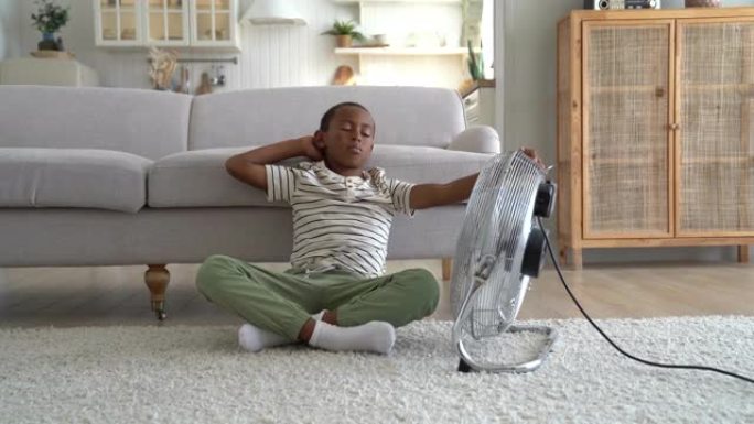 非裔美国男孩坐在电扇旁，孩子在家受热