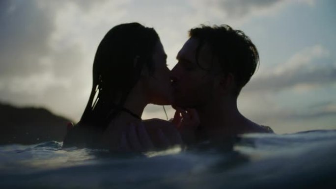 浪漫的异性恋夫妇在日落时一起在海里游泳。在水中接吻