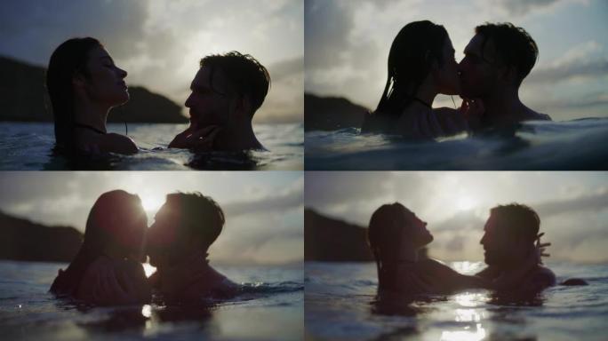 浪漫的异性恋夫妇在日落时一起在海里游泳。在水中接吻