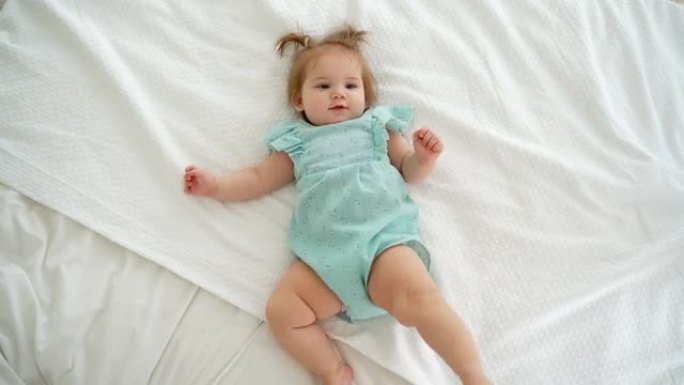 可爱的高加索女婴的肖像，辫子躺在床上看着相机。儿童商品广告。顶视图