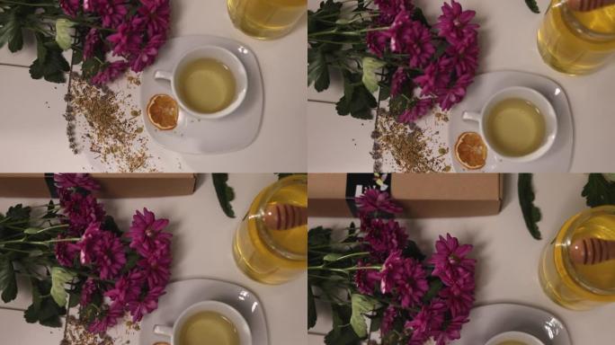 桌子上的陶瓷杯茶的高角度视图，桌子上放着草药，蜂蜜罐，鲜花