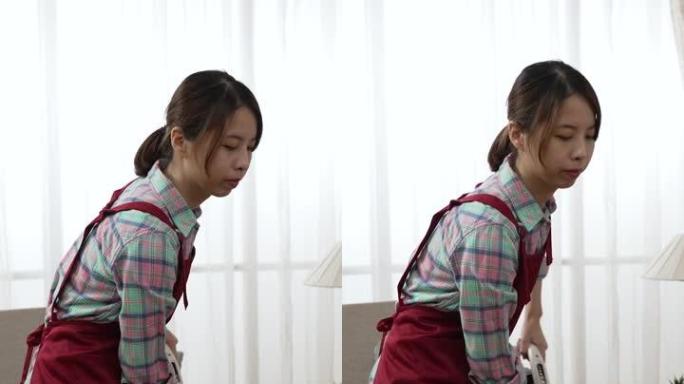 垂直屏幕: 亚洲中国妇女在室内用吸尘器清除地毯上的污垢。优雅的女佣在明亮的客厅里做家务时穿着围裙