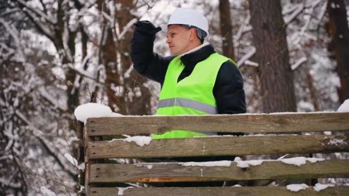 戴着安全帽和防护背心的肖像林务员在寒冷冰冻的冬天从木制观察塔四处观看