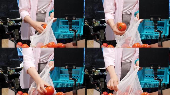 商店里的女人选择成熟的西红柿，然后将它们折叠成棉布袋作为杂货。拒绝塑料，并使用可重复使用的袋子在市场