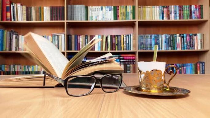 在经典图书馆的木桌、眼镜和金色咖啡杯上预订。风翻页。背景书架。