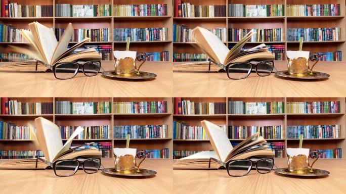 在经典图书馆的木桌、眼镜和金色咖啡杯上预订。风翻页。背景书架。