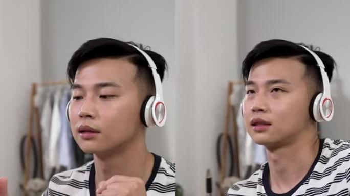 垂直视频: 分心的亚洲年轻人从家里学习，正在玩笔像鼓棒，同时在卧室的办公桌上听耳机上的流行歌曲。