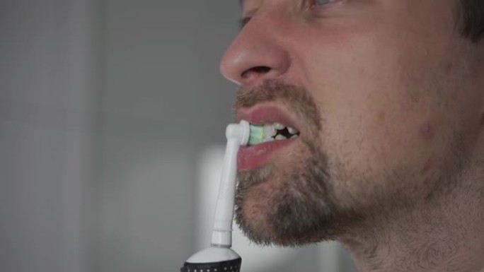 用现代电动牙刷刷牙和美白牙齿的主题。一名男子用超声波牙刷清洁牙齿的特写镜头。早上例行公事，口腔卫生。