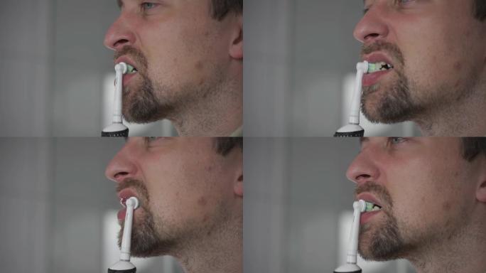 用现代电动牙刷刷牙和美白牙齿的主题。一名男子用超声波牙刷清洁牙齿的特写镜头。早上例行公事，口腔卫生。
