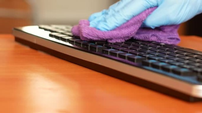 一只戴着医疗手套的手用抹布擦拭电脑键盘。在大流行中消毒个人计算机与细菌的关系。桌面上的清洁度。医用键
