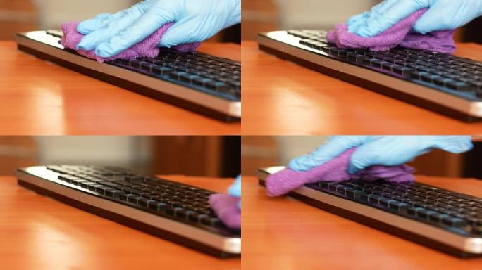 一只戴着医疗手套的手用抹布擦拭电脑键盘。在大流行中消毒个人计算机与细菌的关系。桌面上的清洁度。医用键