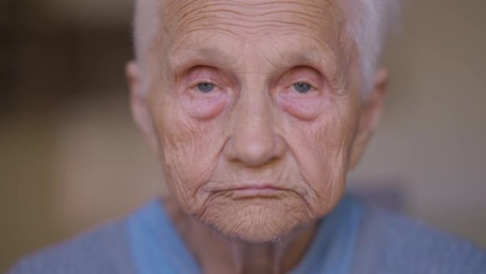灰色眼睛看着相机的老妇人的特写前视。在室内摆姿势的悲伤严肃的白种人白发退休人员的头像。