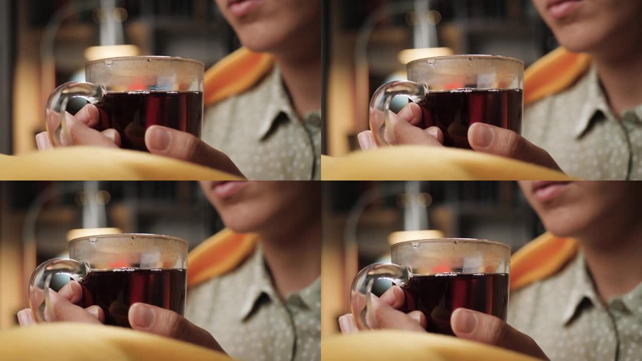 女人喝茶。女性的手在透明的杯子里拿着热茶。特写