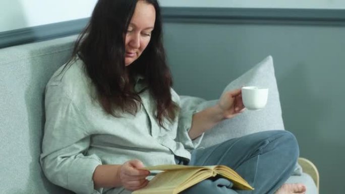 订婚的女人正在看书，坐在家里的沙发上喝咖啡。