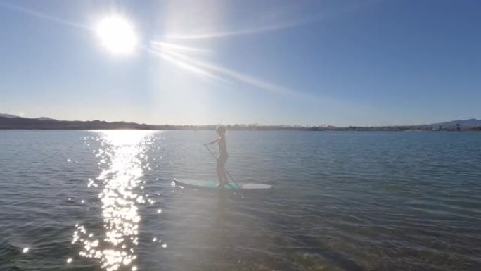 年轻的女飞行员在宁静的湖上站起来划桨板 (SUP)