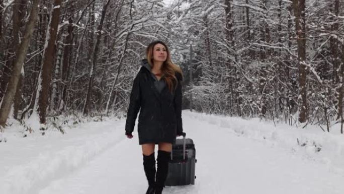 亚洲女性带着手提箱沿着白雪皑皑的森林道路旅行