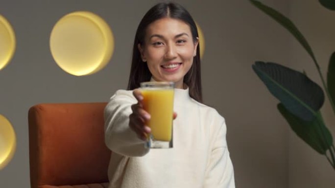 美丽的亚洲女人手里拿着一杯橙汁看着镜头