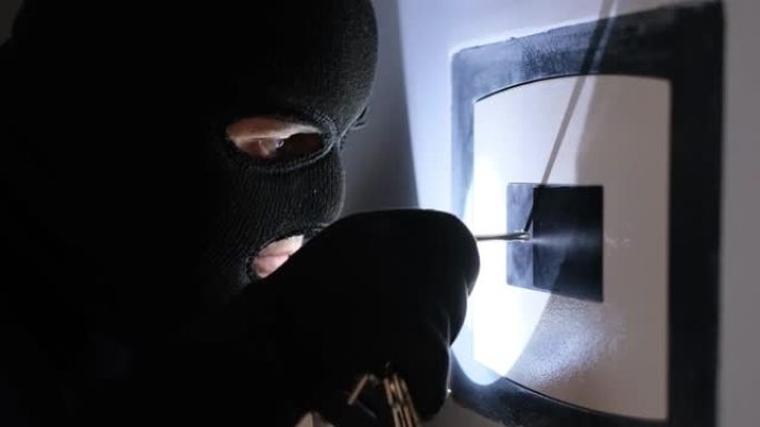 一个戴着黑色面具的强盗打开保险柜，偷走了钱。公寓的小偷。撬开保险箱