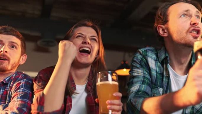 一群年轻人，男人和女人在酒吧看比赛，喝啤酒。球迷情绪激动地为最喜欢的运动队加油。