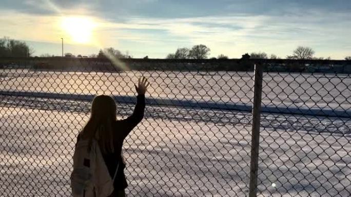 年轻女孩站在链节围栏上，看着积雪覆盖的校园