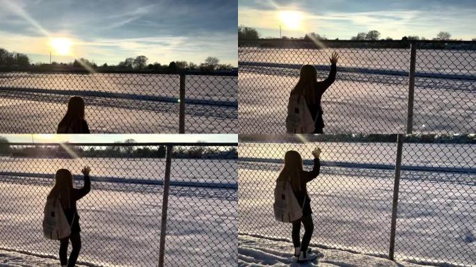 年轻女孩站在链节围栏上，看着积雪覆盖的校园
