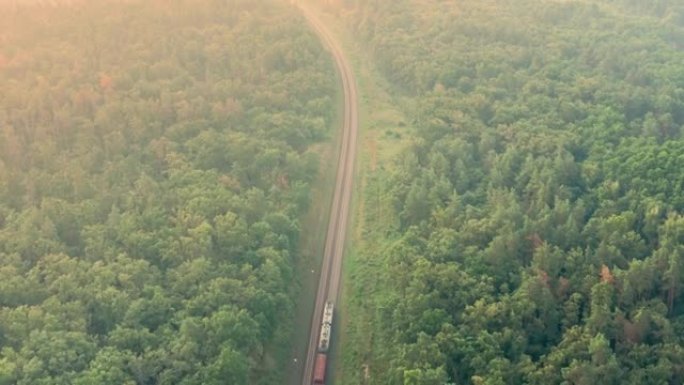 货运火车在绿色的林木之间走得很远-空中进入无人机射击。