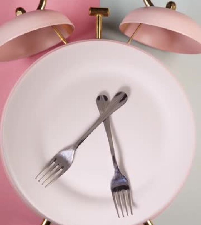 闹钟和带有叉子和刀子的旋转板的垂直视频。吃饭时间，饮食或间歇性禁食概念