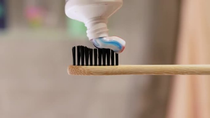 牙膏涂在牙刷上。浴室里的bokeh背景特写。牙齿清洁概念。从管子中挤出牙膏