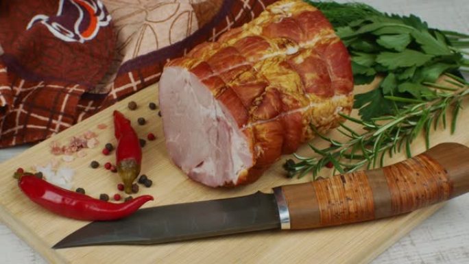 传统火腿在木砧板上刻刀，五颜六色五香果，红辣椒，欧芹，莳萝和罗勒猪肉美味的肉类小吃的概念。